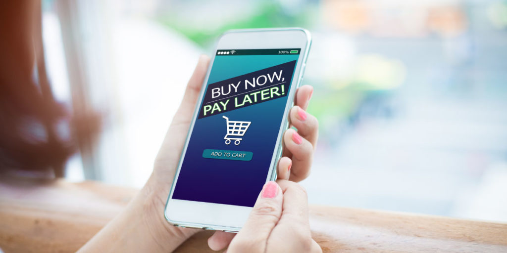Hand holding cellphone with Buy Now Pay Later displayed at checkout cart online.